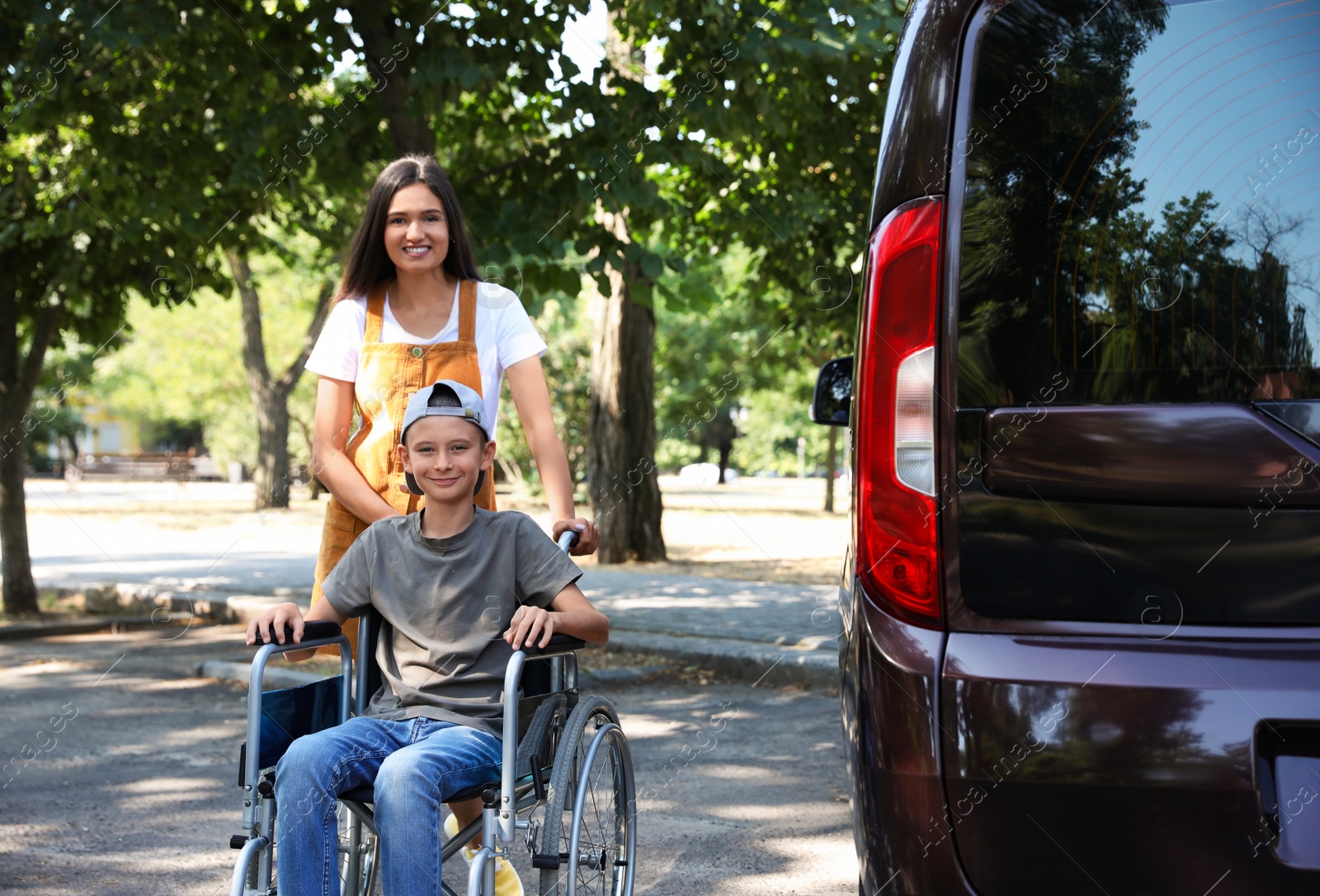 Photo of Young woman with boy in wheelchair near van outdoors