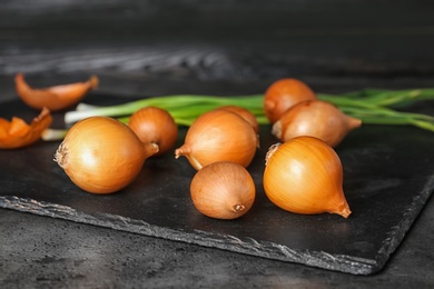 Slate plate with fresh ripe onions on table