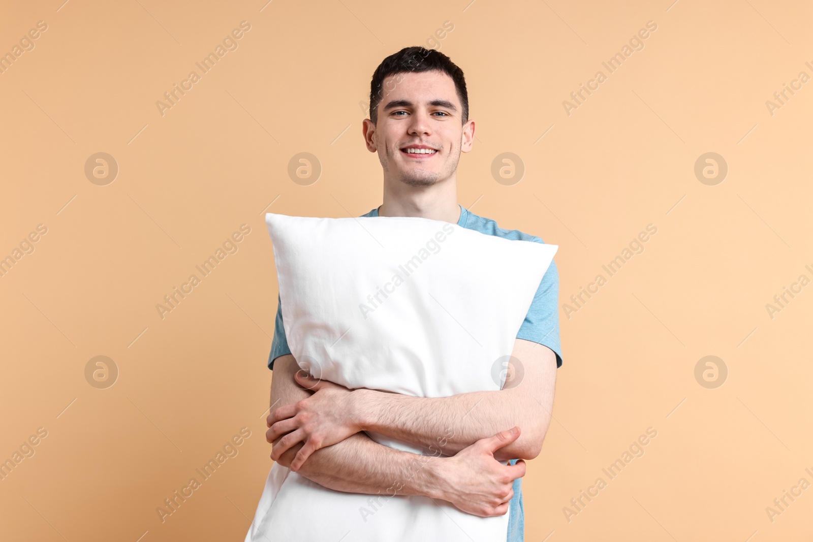 Photo of Happy man in pyjama holding pillow on beige background