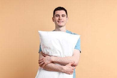 Photo of Happy man in pyjama holding pillow on beige background