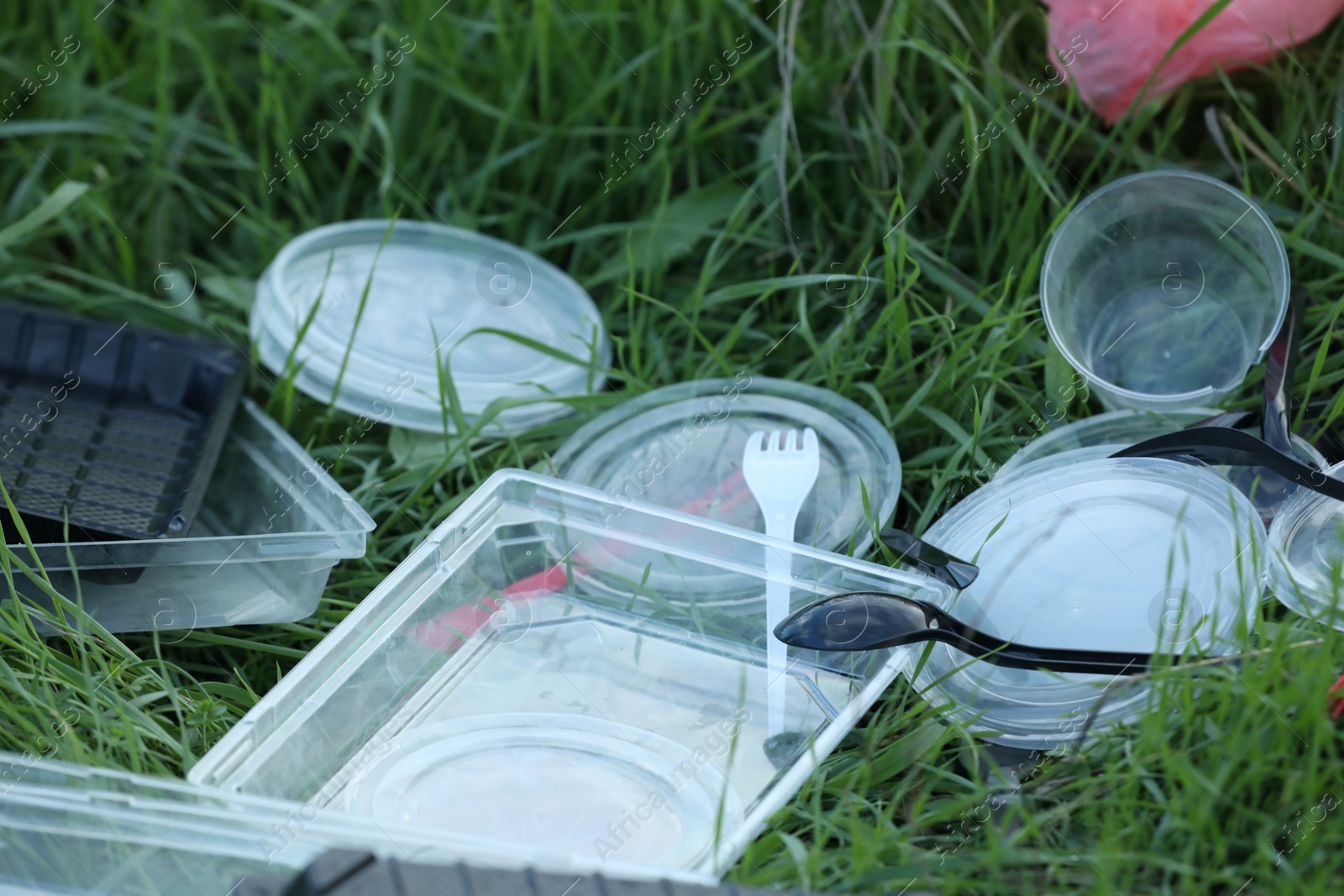 Photo of Used plastic tableware on grass outdoors, closeup. Environmental pollution concept