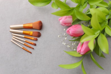 Photo of Makeup brushes and flowers on grey background