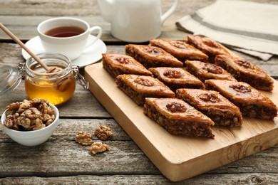 Photo of Delicious sweet baklava with walnuts, honey and hot tea on wooden table