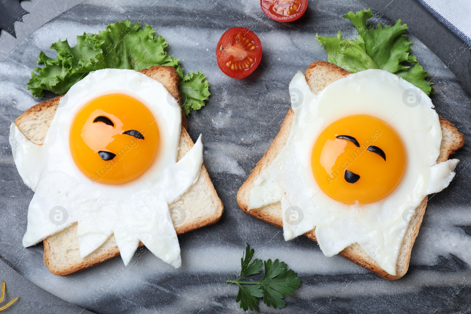 Photo of Halloween themed breakfast served on black table, flat lay. Tasty toasts with fried eggs in shape of ghost