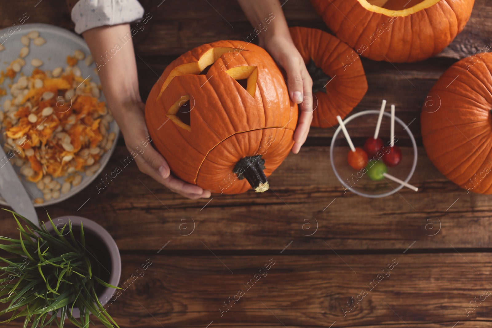 Photo of Woman with pumpkin jack o'lantern at wooden table, top view. Halloween celebration