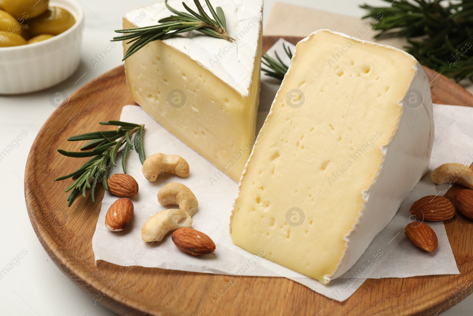 Photo of Plate with pieces of tasty camembert cheese, nuts and rosemary on table, closeup