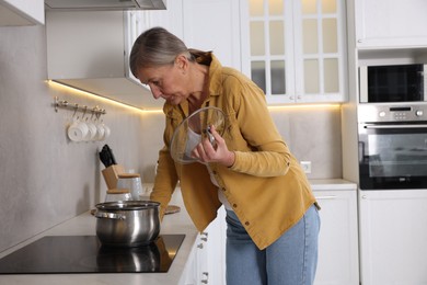 Photo of Menopause. Woman suffering from hot flash while cooking in kitchen
