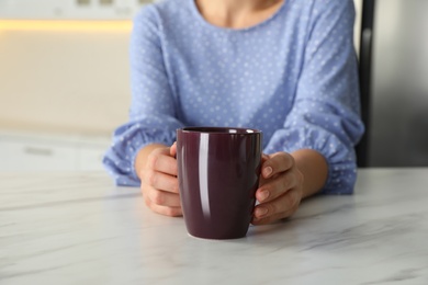 Photo of Woman with dark purple cup at table indoors, closeup