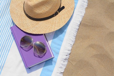 Beach towel with book, sunglasses and straw hat on sand, flat lay. Space for text