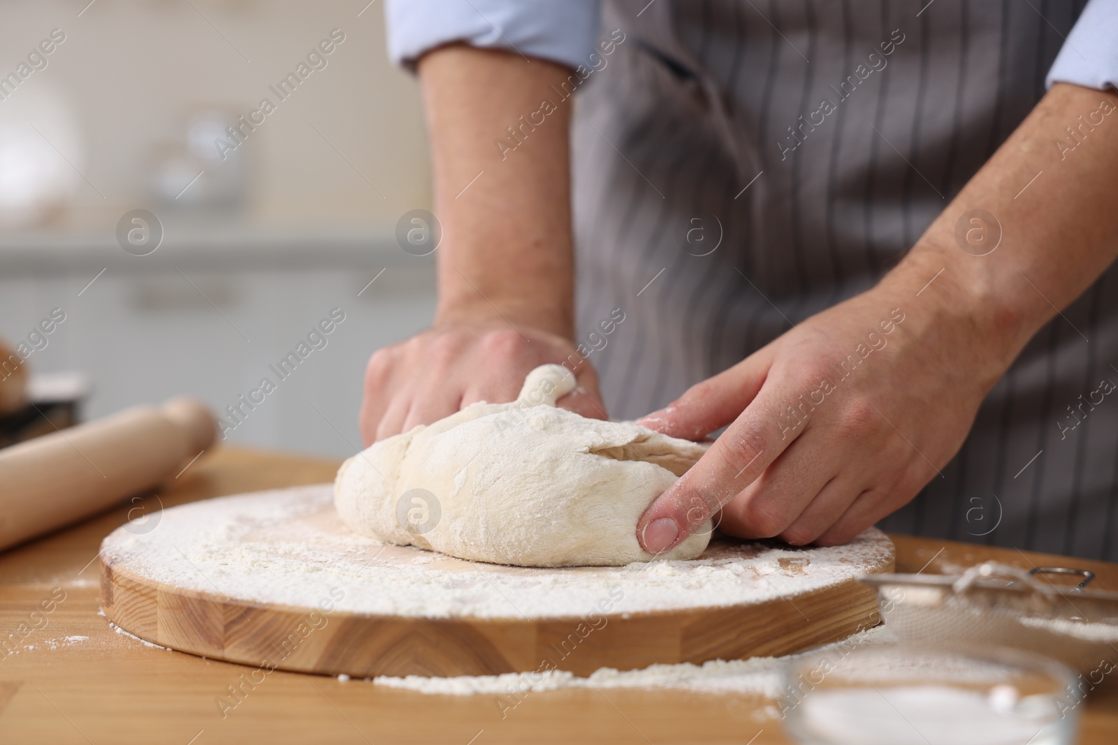 Photo of Making bread. Man kneading dough at wooden table in kitchen, closeup