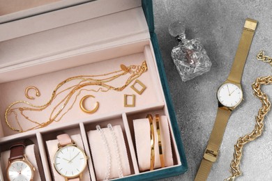 Photo of Jewelry box with many different accessories and perfume on light grey table, flat lay