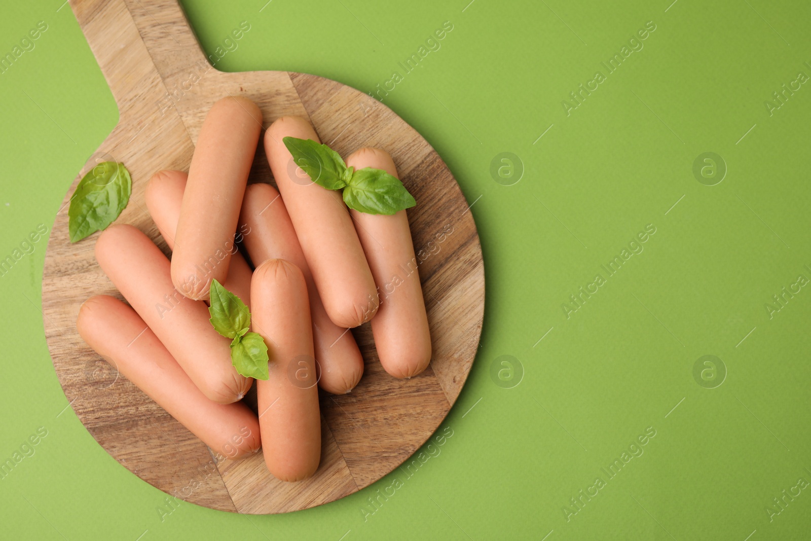 Photo of Delicious boiled sausages and basil on green table, top view. Space for text