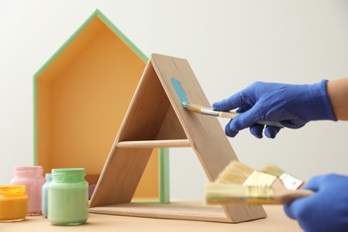 Photo of Decorator painting pyramid shaped shelf with brush at wooden table, closeup. Interior element