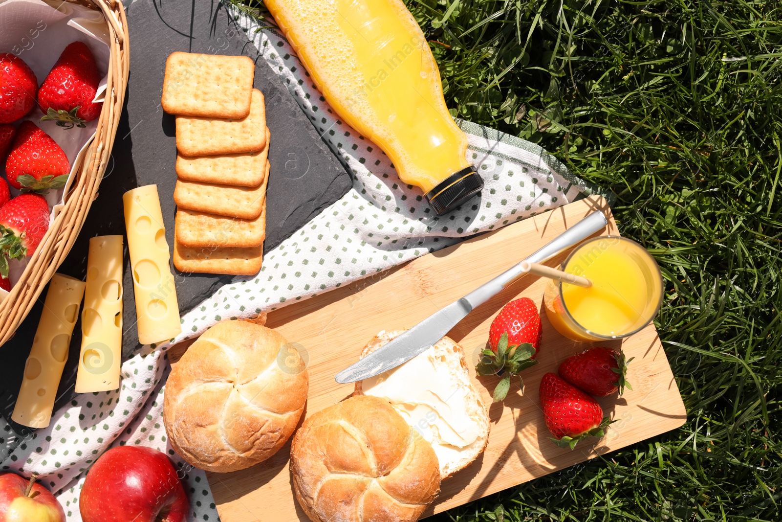 Photo of Blanket with juice and snacks for picnic on green grass, flat lay