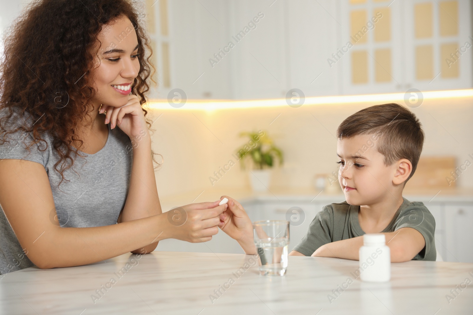 Photo of African-American woman giving vitamin pill to little boy in kitchen