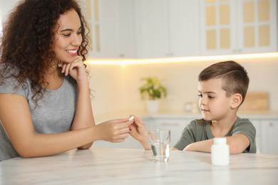 African-American woman giving vitamin pill to little boy in kitchen