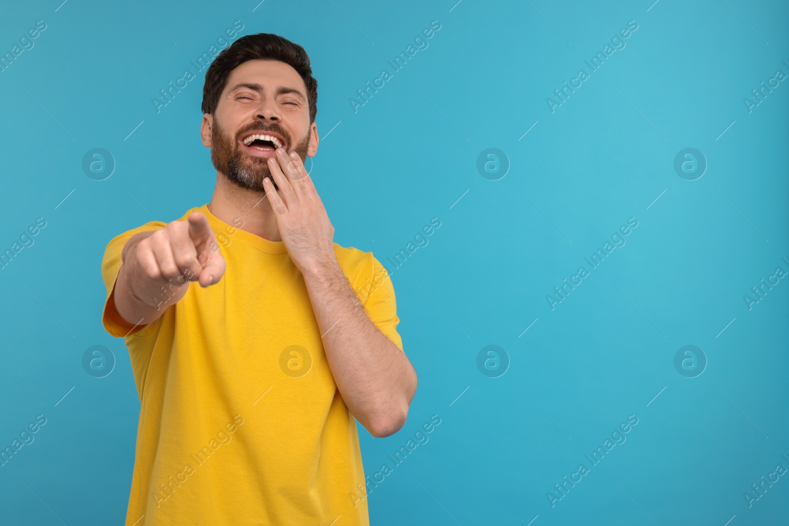 Photo of Handsome man pointing at something and laughing on light blue background. Space for text