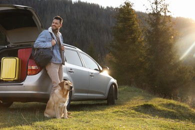 Happy man and adorable dog near car in mountains. Traveling with pet