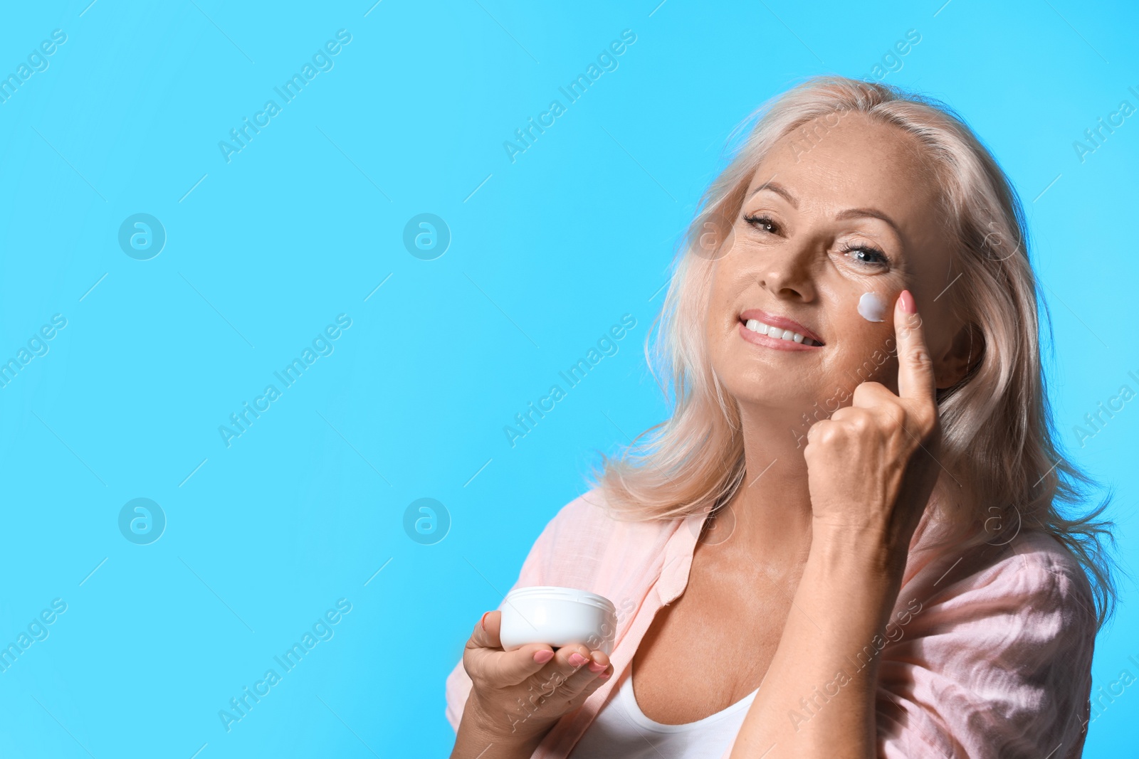 Photo of Portrait of beautiful mature woman with perfect skin applying cream against light blue background. Space for text