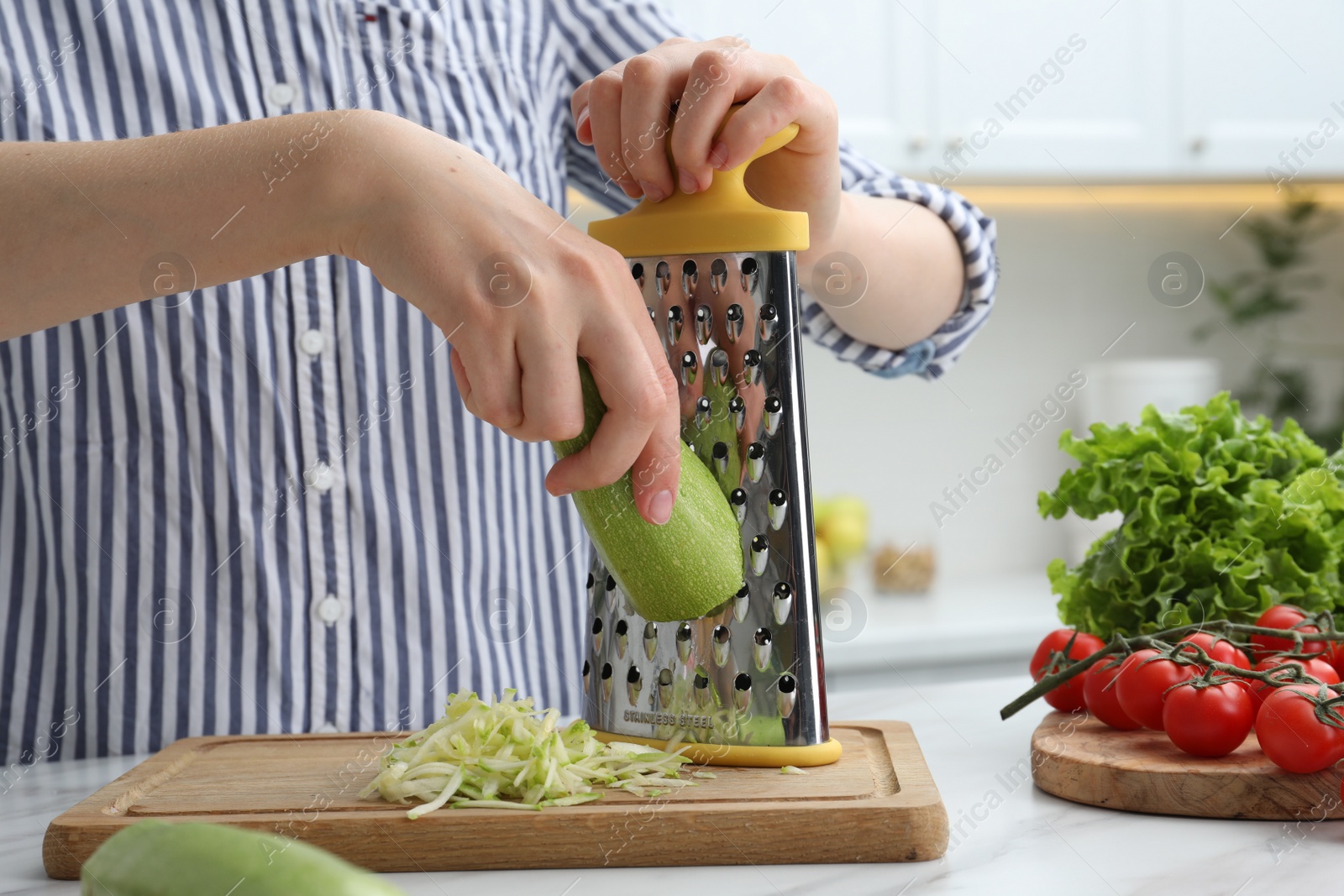 Photo of Woman grating zucchini at kitchen table, closeup