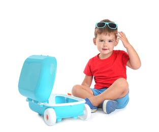 Photo of Cute little boy sitting with blue suitcase on white background
