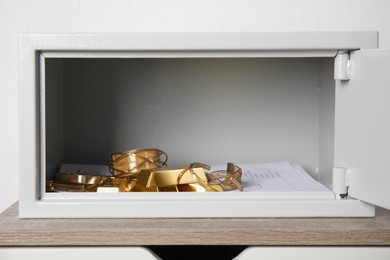 Photo of Open steel safe with gold bars and jewelry on wooden table against white background