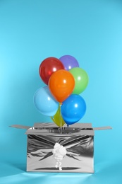 Gift box with bright air balloons on color background