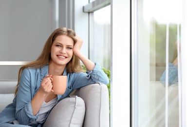 Young beautiful woman drinking morning coffee near window at home