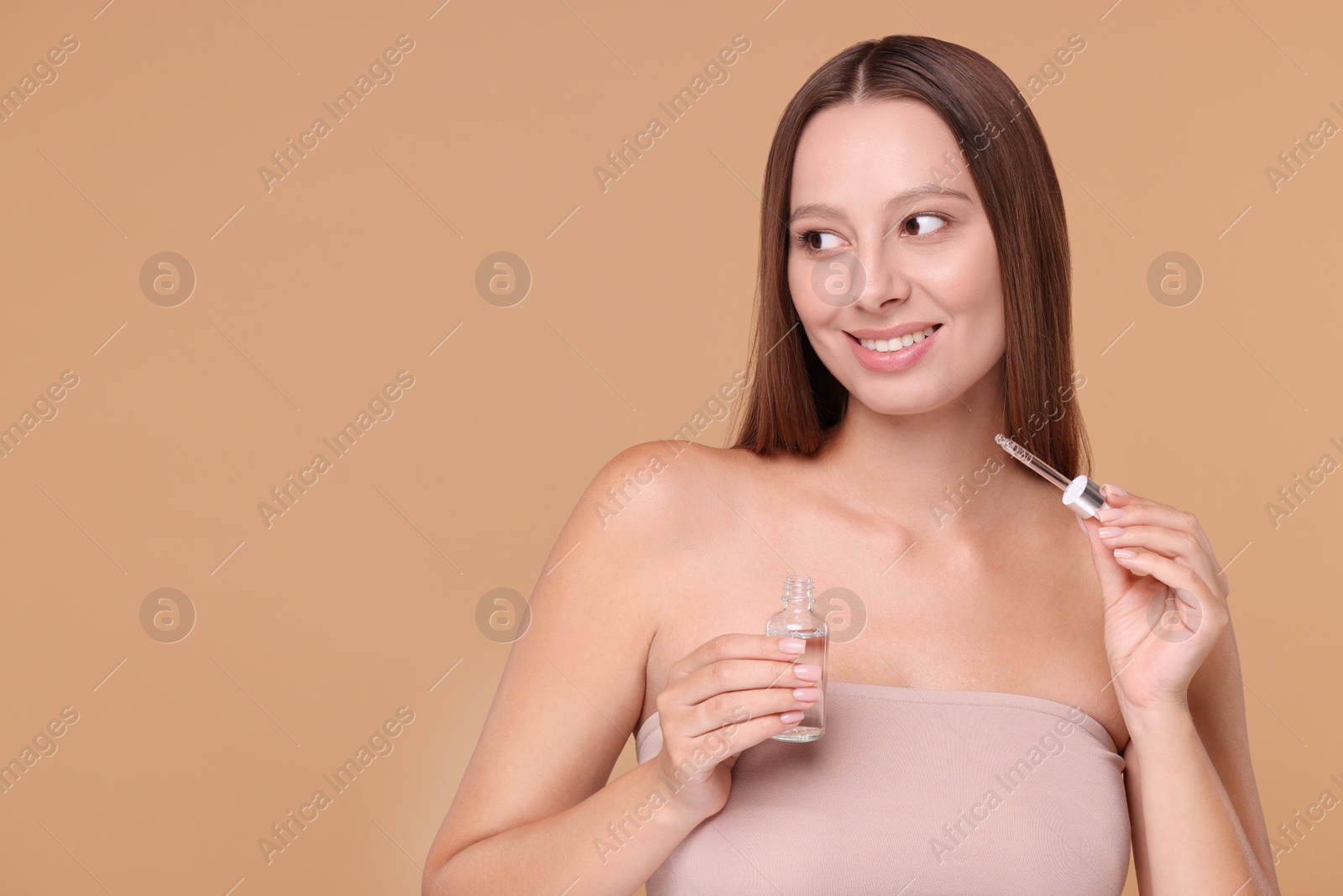Photo of Beautiful woman holding bottle of serum and dropper on beige background, space for text