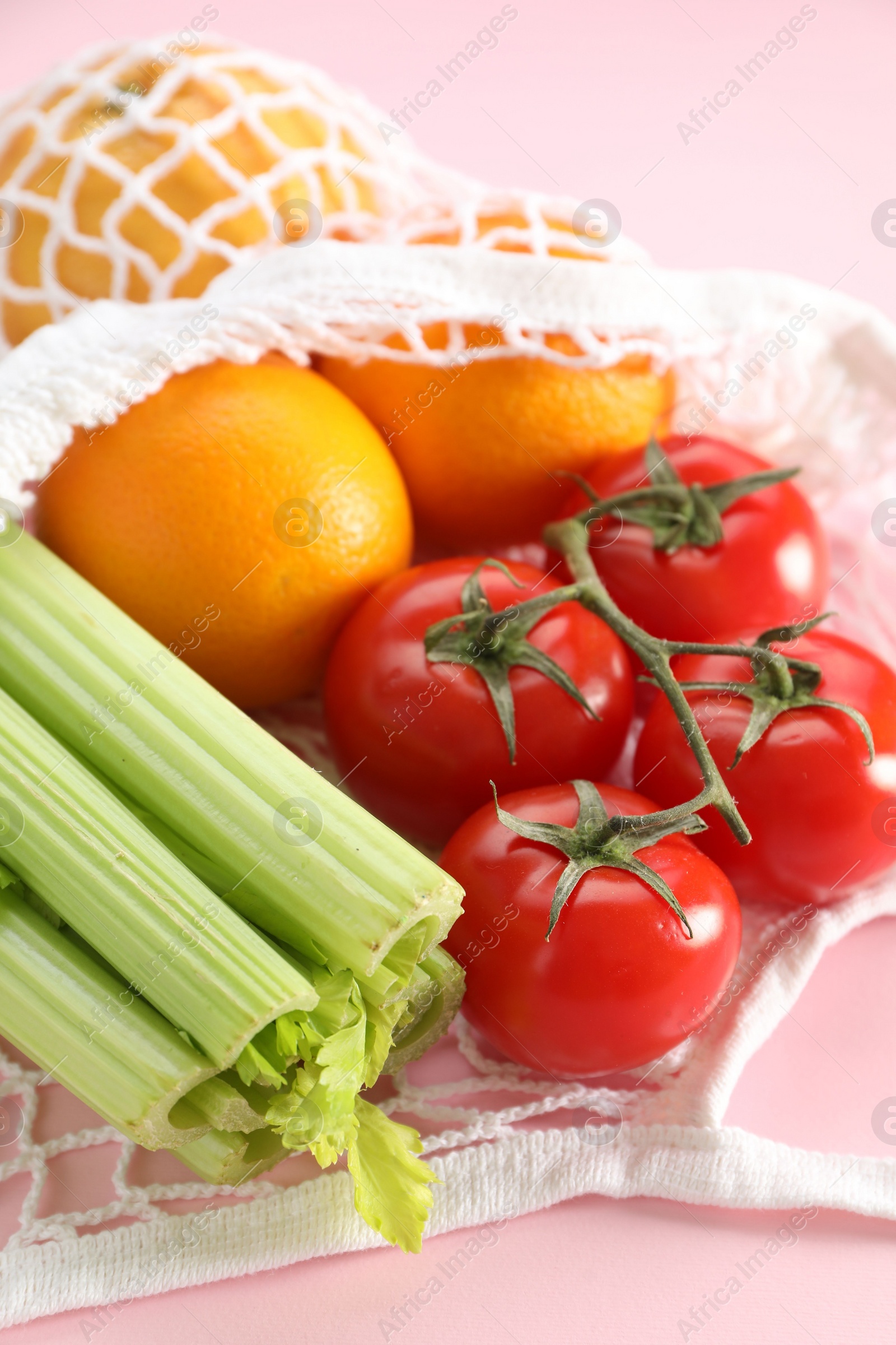 Photo of String bag with different vegetables and fruits on pink background, closeup