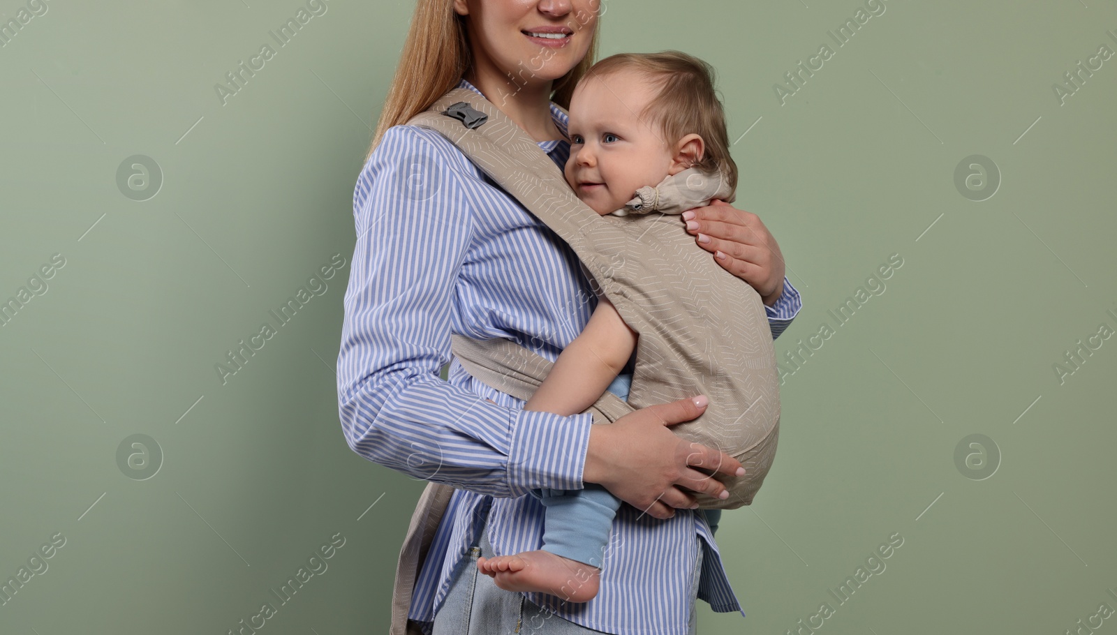 Photo of Mother holding her child in sling (baby carrier) on olive background, closeup