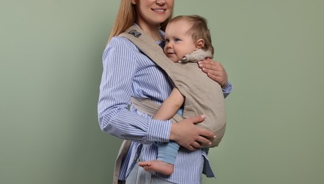 Photo of Mother holding her child in sling (baby carrier) on olive background, closeup