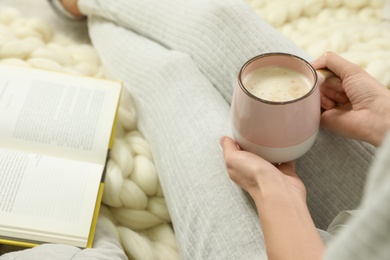 Woman with cup of coffee and book sitting on soft plaid, closeup