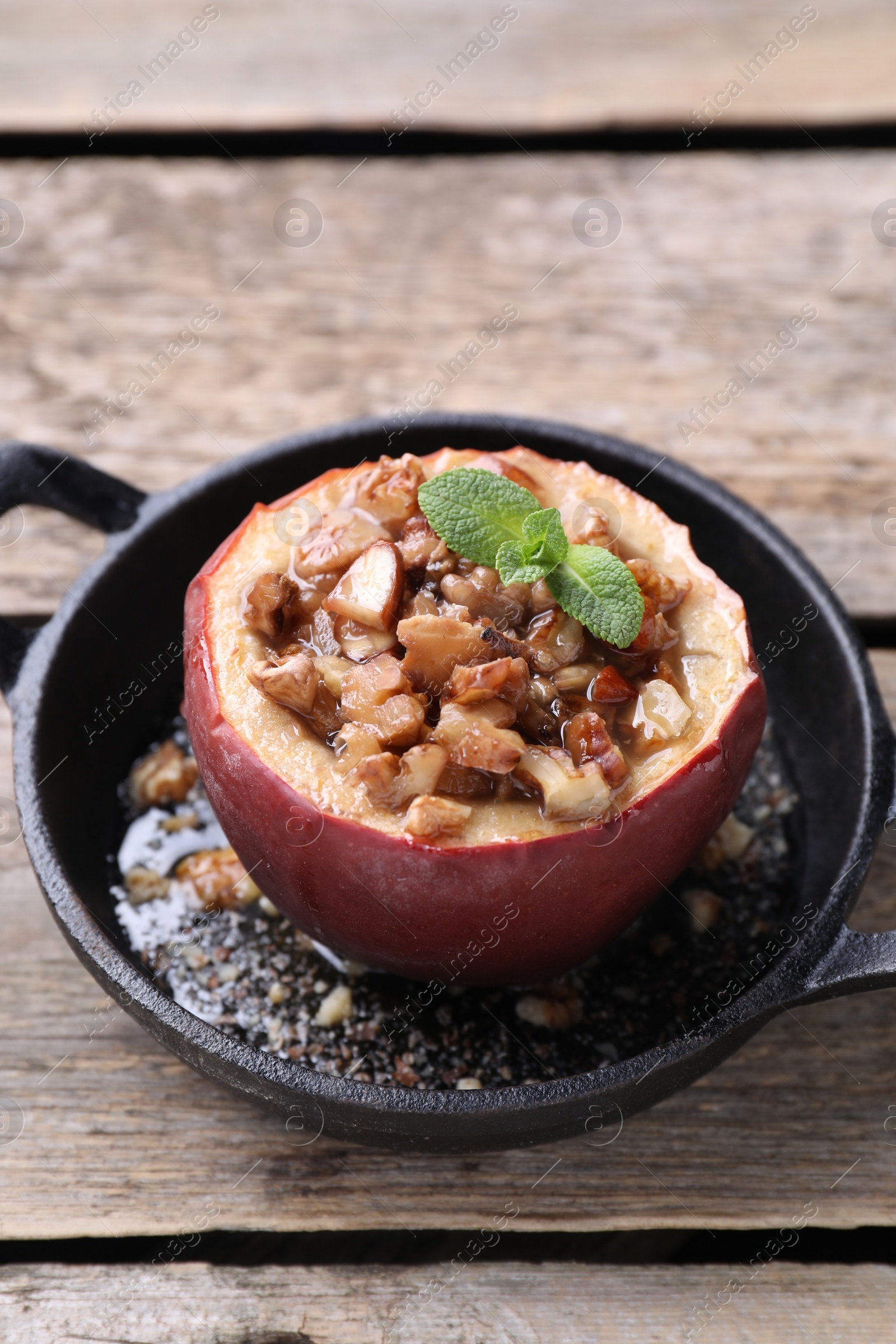 Photo of Tasty baked apple with nuts, honey and mint in baking dish on wooden table, closeup