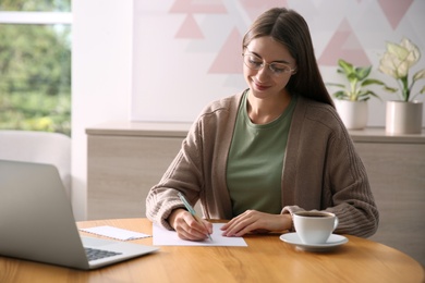 Photo of Woman writing letter at wooden table in room