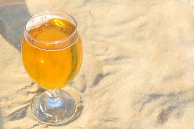 Glass of cold beer on sandy beach, closeup. Space for text