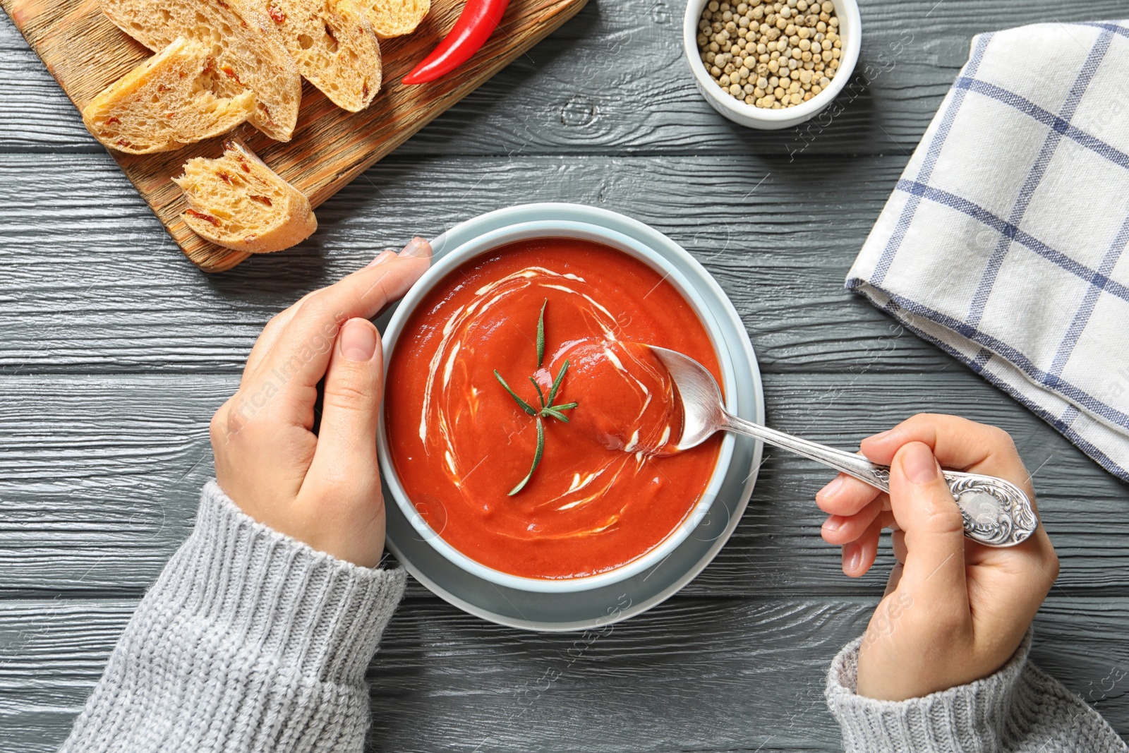 Photo of Woman eating fresh homemade tomato soup at wooden table, top view