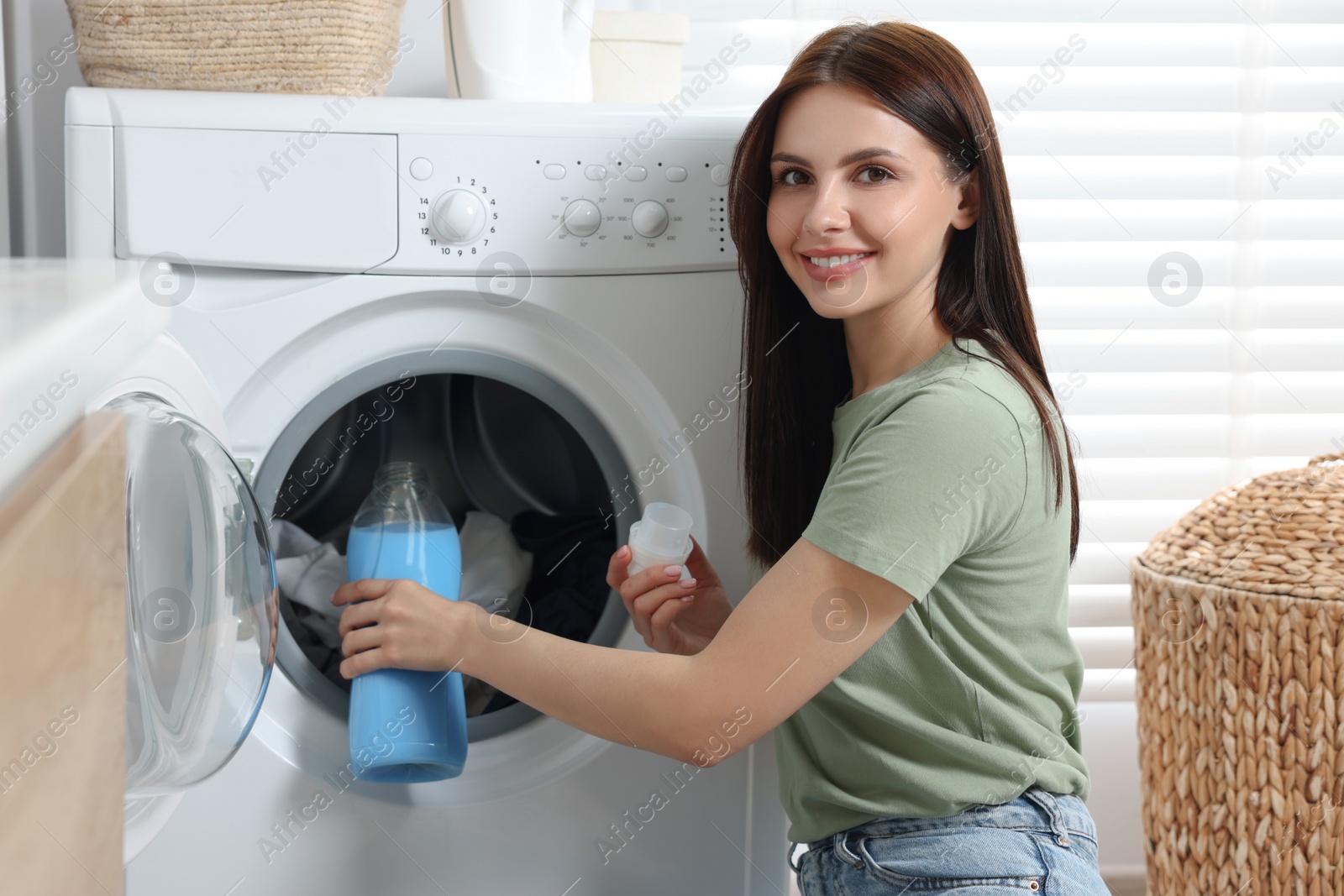 Photo of Woman pouring fabric softener into washing machine in bathroom