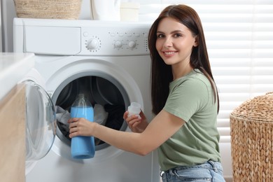 Photo of Woman pouring fabric softener into washing machine in bathroom