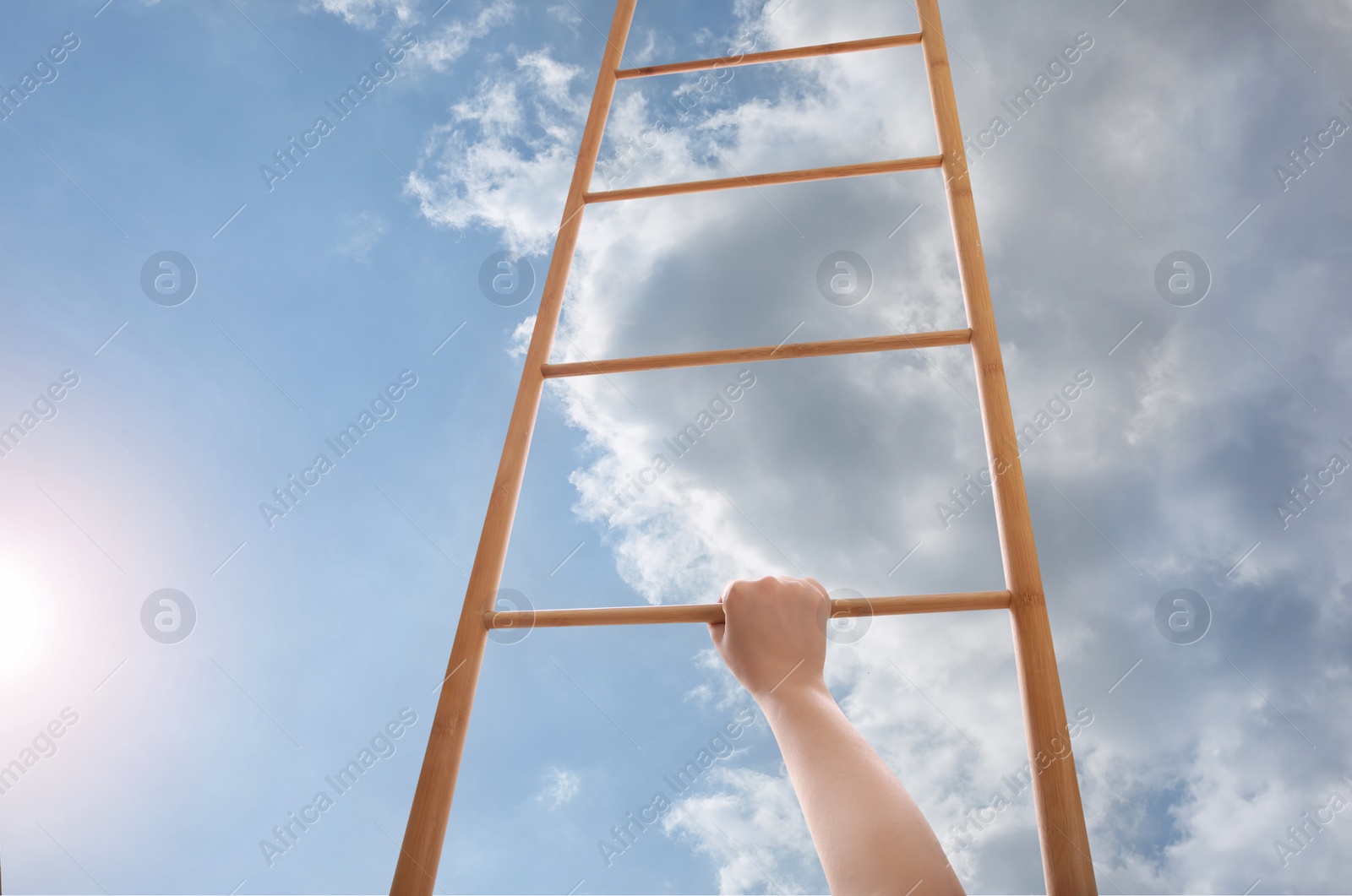 Image of Woman climbing up wooden ladder against blue sky with clouds, closeup