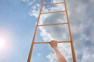 Woman climbing up wooden ladder against blue sky with clouds, closeup