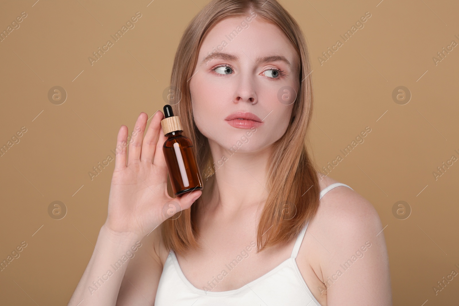 Photo of Beautiful young woman with bottle of essential oil on brown background