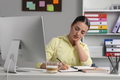 Young woman suffering from neck pain while working at table in office
