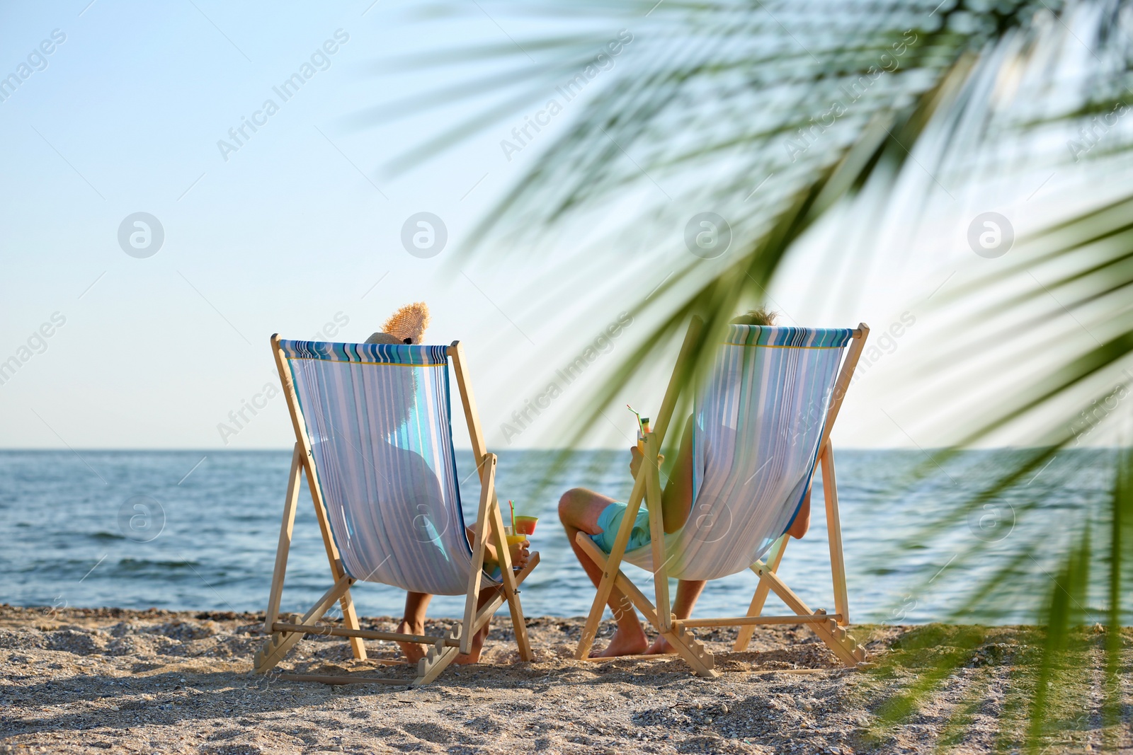 Photo of Young couple with cocktails in beach chairs at seacoast