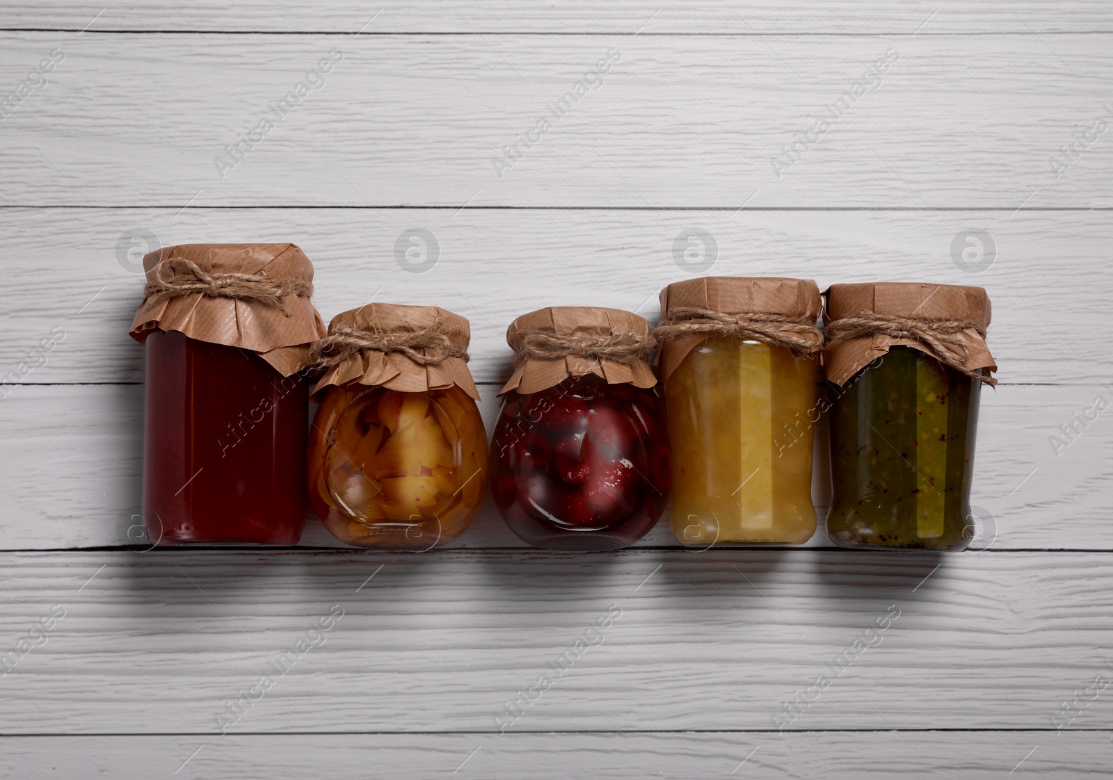 Photo of Jars with preserved fruit jams on white wooden table, flat lay