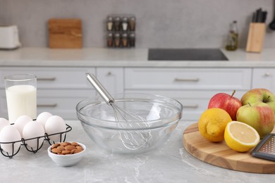 Photo of Metal whisk, bowl and different products on gray marble table in kitchen