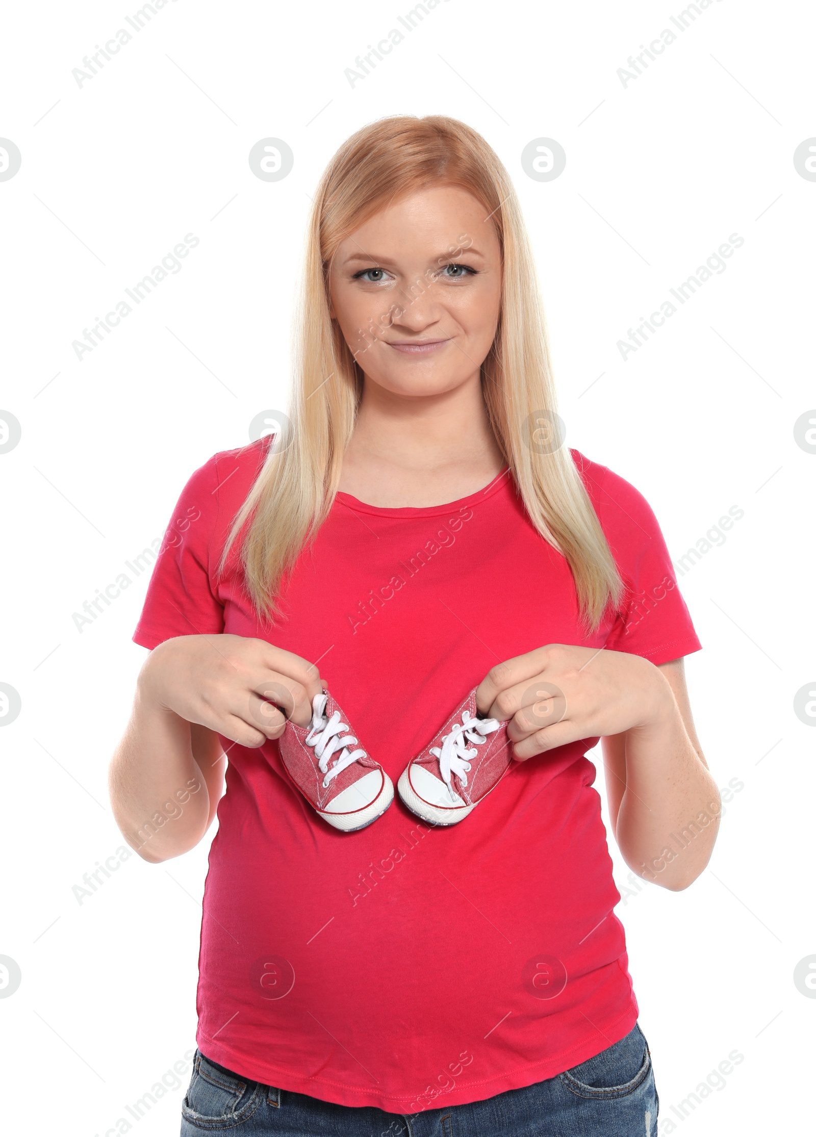 Photo of Beautiful pregnant woman holding baby booties near tummy on white background