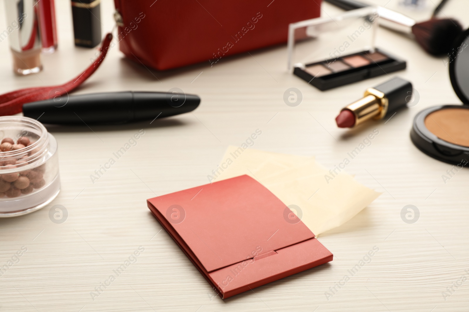 Photo of Package with facial oil blotting tissues and makeup products on white wooden table. Mattifying wipes