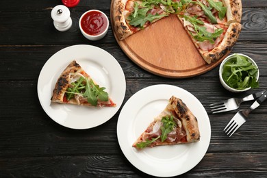 Tasty pizza with meat and arugula on black wooden table, flat lay