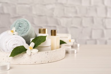 Beautiful jasmine flowers, towels and skin care products on white wooden table, space for text